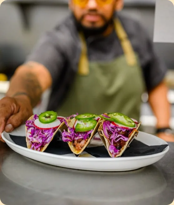 Chef reaching across a plate of tacos